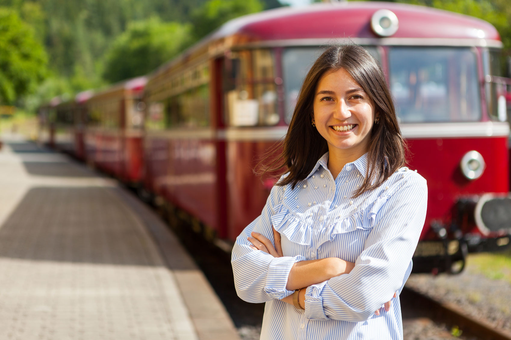 Lächelnde junge Frau vor rotem historischen Zug mit Text 'Werde Teil der AKE-Eisenbahntouristik'