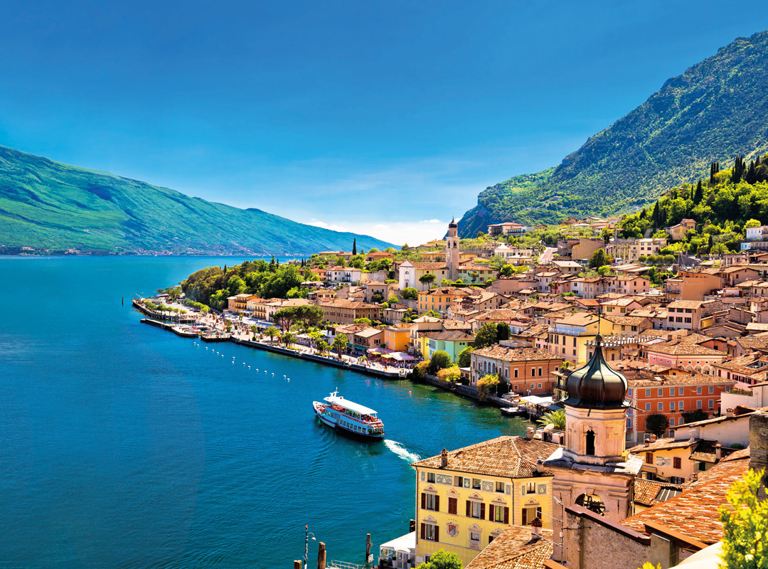 Blick auf eine italienische Küstenstadt mit Boot auf dem See und Bergen im Hintergrund