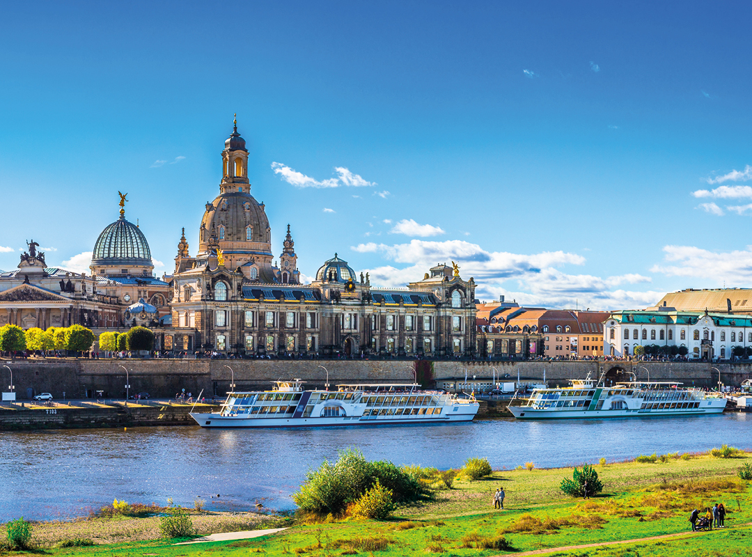 Blick über die Elbe auf die historische Altstadt von Dresden mit der Frauenkirche, der Brühlschen Terrasse und Ausflugsschiffen auf dem Fluss.