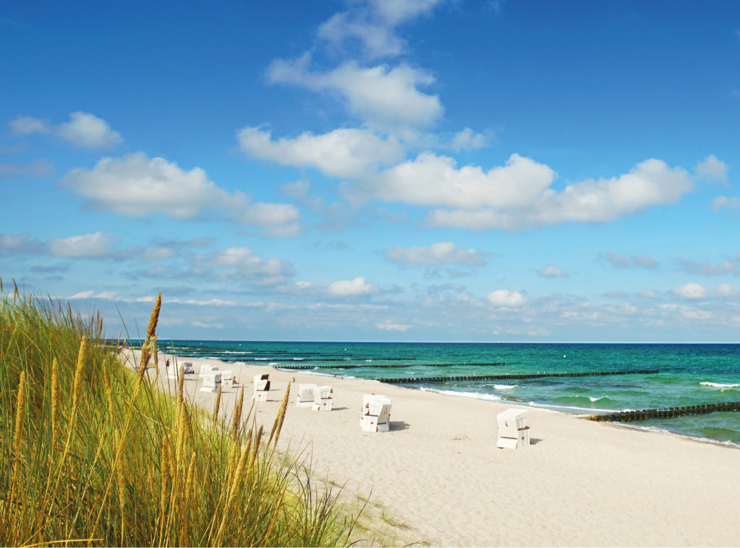 Weißer Sandstrand auf Sylt an der Nordsee mit Strandkörben, bewachsenen Dünen und türkisblauem Meer.